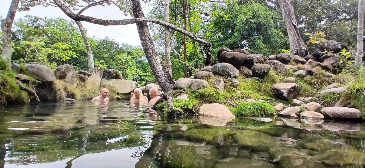 Guests soaking in a natural hot spring pool at Caldera, framed by boulders and cloud forest